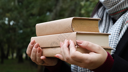 在秋季公园的背景下 一位身穿黑色外套和灰色围巾的年轻女子手里拿着一叠书 在露天 教育 一个在大学读书的女孩的亲密双手图片