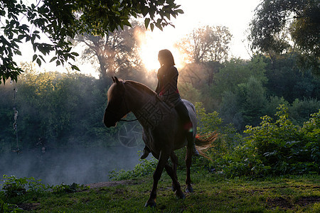 年轻女子骑马在美丽的风景上 清晨雾雾时湖清澈 日出图片