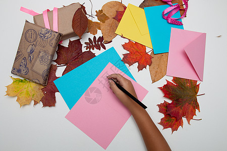 孩子们的手写在一张粉红色的感恩节贺卡 礼品盒 信封和秋叶上白桌 复制空间 顶视图片