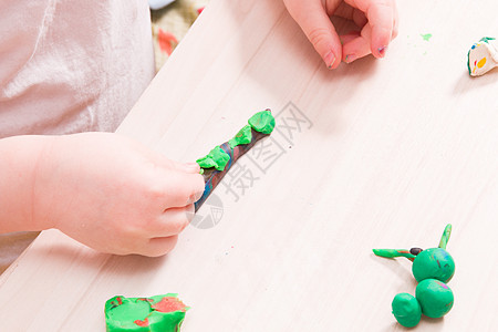 一个小孩在木桌上用绿色橡皮泥雕刻毛毛虫 手部精细运动技能的发展 在家里和孩子玩耍 前景中用橡皮泥雕刻毛毛虫材料学习黏土想像力教育图片