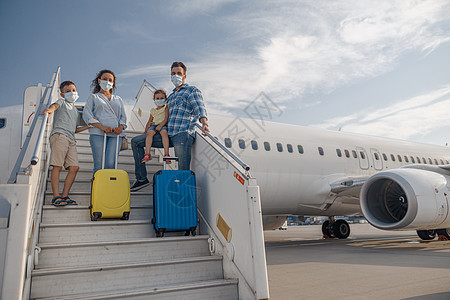 幸福的家庭戴保护面罩 父母有两个小孩的父母站在空中 白天登上飞机日光日光日照行李面具旅行妻子男生快乐假期父亲童年游客图片