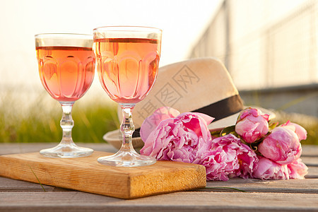 两杯玫瑰葡萄酒和粉红小马花束 美味的清新饮料 盛开花朵和男子帽太阳新娘玻璃派对夫妻植物学码头植物群帽子玫瑰图片