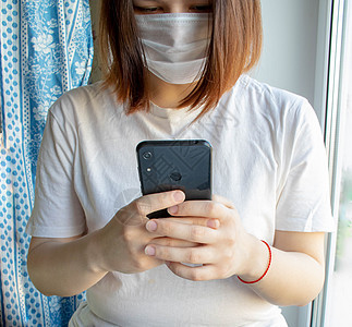 一名身份不明的女童脸上有医疗面具 手和手机 窗户附近的房子图片