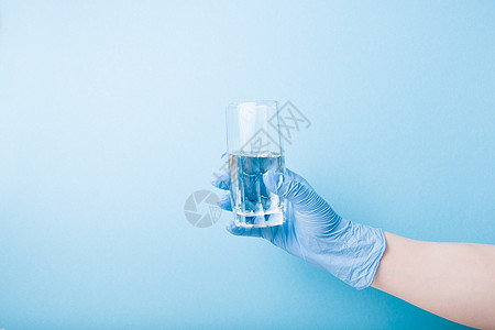 蓝色一次性医疗手套上装着一个玻璃杯 有水 蓝本底空间图片