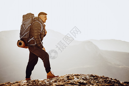 在山顶站立的徒步旅行设备中的男性背包男远足活动顶峰游客耐力成就岩石地平线农村运动图片
