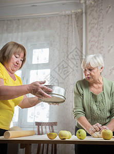 两个老年妇女在家里做苹果小馅饼 桌上有面粉擦拭图片