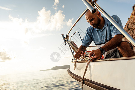 日落时 美国年轻水手在海上帆船上绑绳子血管绳索队长男人全体闲暇巡航男性休闲装航程图片