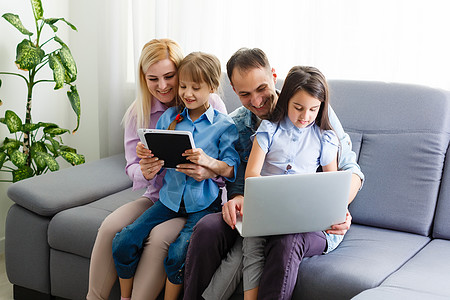 幸福的四口之家和可爱的小孩喜欢使用平板电脑 看卡通片 进行网络视频通话或在线购物 看着电脑屏幕坐在家里购买设备通讯男人女士社交父图片