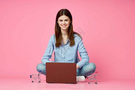 妇女坐在地板上 有笔记本电脑 购物娱乐和粉红色背景电子商务店铺地面银行业女士技术信用女性互联网白色图片