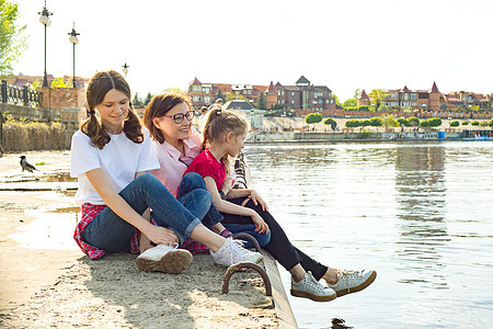 母亲和两个女儿的户外肖像 看着水 背景自然 公园 河流图片