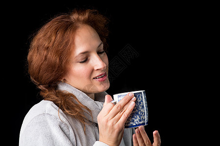 微笑的女人拿着瓷杯 在摄影棚里拍照女士情感冒充享受女孩成人杯子头发饮料早餐图片