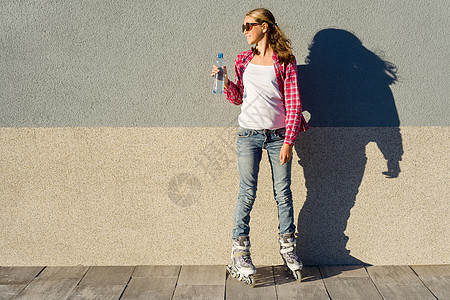 带一瓶水的年轻女孩 在滚滚机里放沙子 背景灰墙 复制空间图片