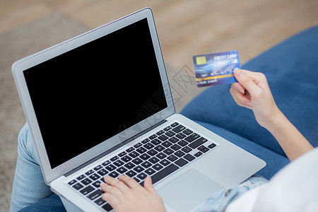 年轻的亚洲女性使用笔记本电脑显示空白屏幕在家里沙发上用信用卡在线购物 女孩购买和使用借记卡付款 电子商务和技术 生活方式概念图片