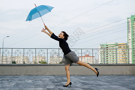 在这座城市的背景下 一只母的在雨伞后面跑来跑去图片