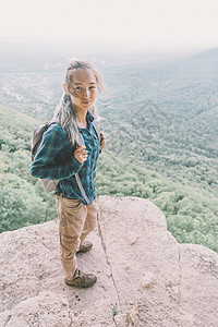 背着背包的旅游女孩站在悬崖上图片