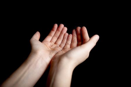 在深黑色背景下乞求或祈祷的张开手势信仰 帮助 崇拜者标志概念图片