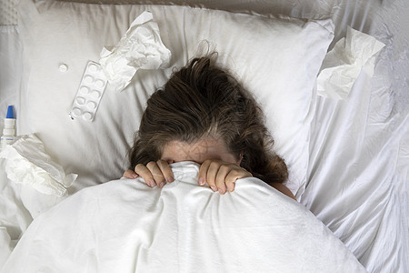 一个生病的年轻女人躺在床上 头盖在毯子下 俯视图旁边放着一堆纸巾 下班回家发烧 白床单咳嗽说谎过敏治疗组织疼痛青少年女性保健感染图片