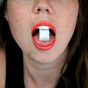 一个女人嘴里舌头上放着糖块的特写不健康的食物 糖果 糖果概念背景图片
