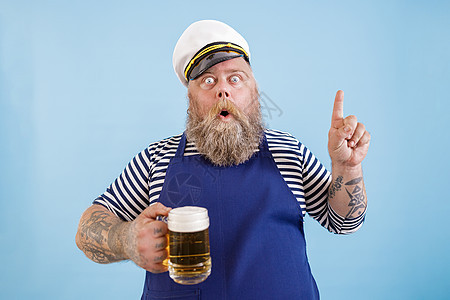 超重的情绪水手拿着啤酒和轻蓝背景的手势图片