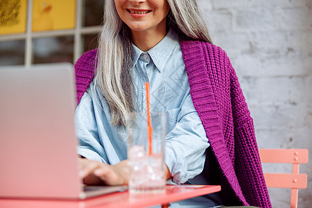 微笑的成年女子坐在咖啡厅露台彩色桌子上的笔记本电脑上工作图片