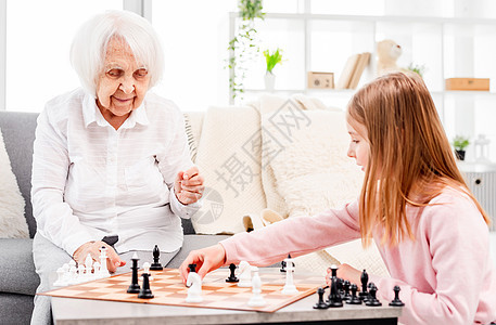 与祖母一起下象棋的女孩竞赛游戏成人学习木板专注白色战略智力房间图片