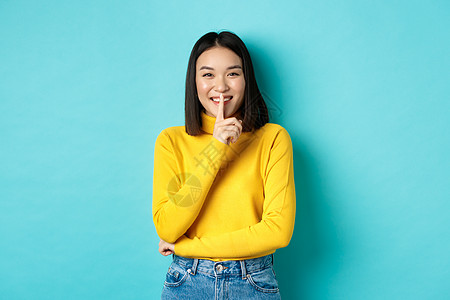 欢快的亚洲女孩要求排队 对着镜头低声尖叫 微笑 保守秘密 站在蓝背景上站立快乐发型商业理发情感交易女性学生成人广告图片