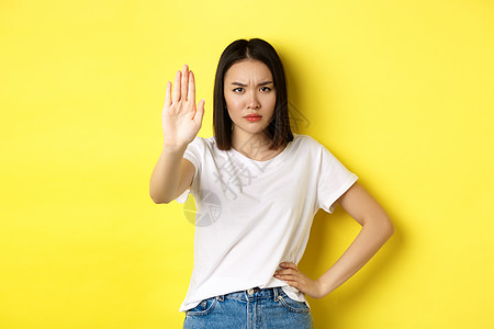 自信而严肃的亚洲女人说不 表现出停止的手势来禁止和警告 与某人持不同意见 对黄色背景感到不满工作室理发女性广告学生快乐青少年促销图片