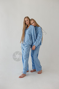 两个漂亮的双胞胎姐妹 长金发长发 穿着白色的白底衣装扮成超大衣服冒充女士家庭金发女郎青少年蓝色工作室套装女孩姐姐图片