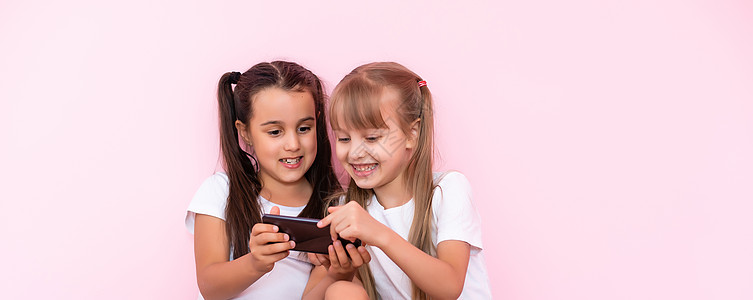 两个小女孩 带着智能手机 在粉红背景上学校喜悦青春期电话童年互联网孩子房子友谊朋友们背景