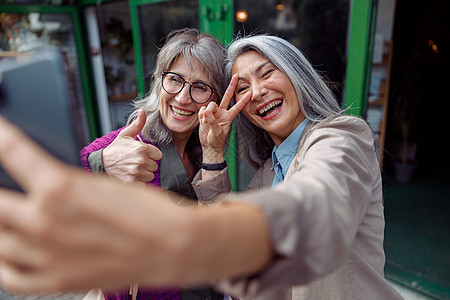 有朋友的迷人成熟亚洲女人 在市街上用电话自拍 和自己玩图片