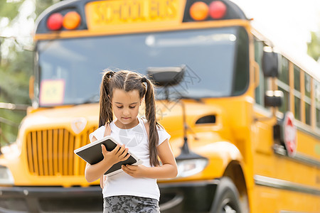 在黄色校车附近有背背包女孩的黄色校车学生快乐笔记本路线小学生童年学习补给品汽车微笑图片