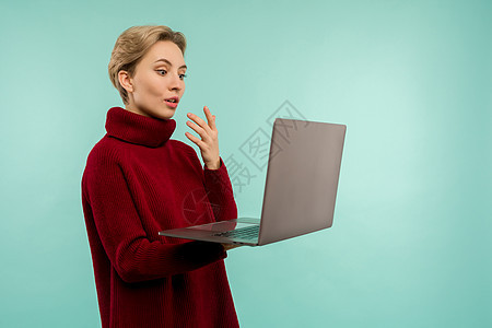 穿着红色毛衣的惊喜女孩看着蓝背景的笔记本电脑屏幕药片手臂成人技术微笑展示键盘空白网络互联网图片