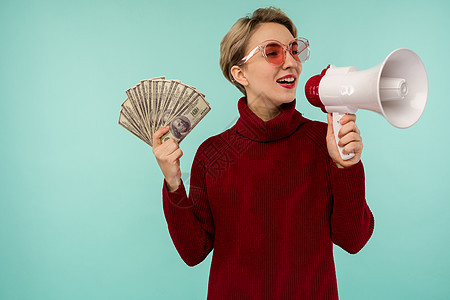 身着粉红墨镜的年轻女子 拿着钱向喇叭大喊大叫现金商业女孩女士扇子财富成功成人女性巨音图片