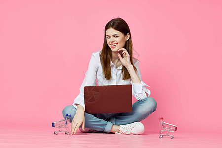 妇女坐在地板上 手持笔记本的在线购物技术粉红色背景店铺白色互联网夫妻信用办公室电子商务女孩电脑女士图片