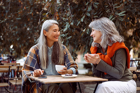 积极成熟的亚洲妇女与在街头咖啡厅桌边休息的好朋友交谈会谈女性街道成人咖啡店快乐幸福朋友格子头发图片