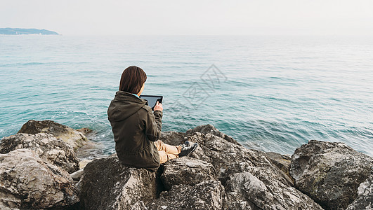 坐在海岸带石板的旅游妇女图片