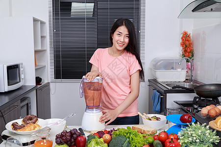 妇女在厨房里用搅拌机做蔬菜冰淇淋橙子排毒萝卜奶昔果汁饮食成人女孩微笑营养图片