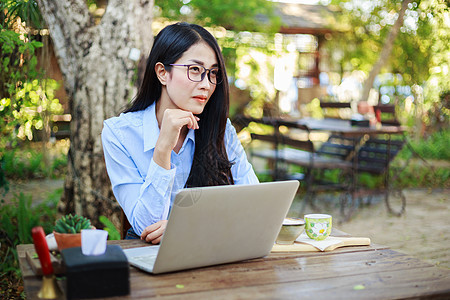 女青年在花园用笔记本电脑和咖啡的肖像桌子女性思维园艺咖啡店技术花园餐厅女孩微笑图片