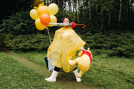 穿黄色雨衣的女人手上握着许多不同的东西 在下雨前的夏天在公园里 然后她就来了图片