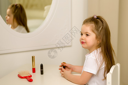 一个小女孩靠近镜子 画着唇唇膏童年嘴唇喜悦女士裙子油漆眼睛头发微笑房间图片