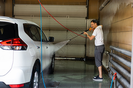 高个子的年轻人 用花园水管把车压在地上男人肥皂泡沫冲洗辉光成人玻璃汽车窗户车辆图片
