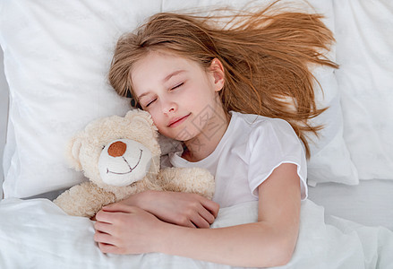 女孩和泰迪熊在床上卧室毯子白色休息拥抱微笑就寝时间枕头童年图片