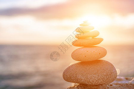 日落时卵石滩上平衡的岩石金字塔 背景上海泡沫的选择性聚焦抽象散景 海沙滩上的禅石冥想水疗和谐平静平衡概念海滩精神温泉海洋石头太阳图片