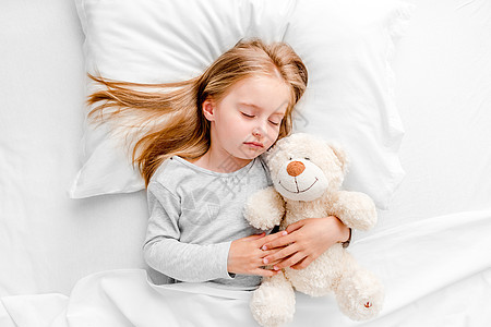 女孩睡在白床上微笑童年女儿玩具孩子唤醒休息白色头发图片