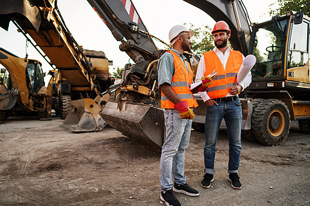 两名男工程师讨论他们站在建筑机械上的工作职员头盔领班安全建筑学工人男性安全帽建设者事故图片