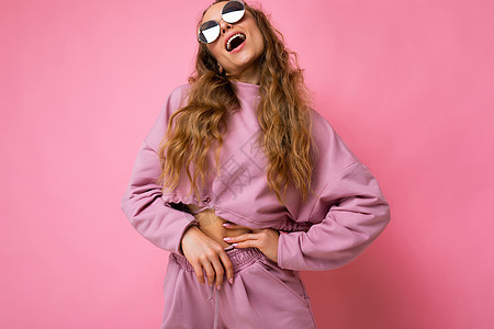 身穿粉红运动衣和时尚墨镜仰望的粉红色背景墙壁上被隔离着 这幅照片来自一位非常正面的金发美女卷发女郎图片