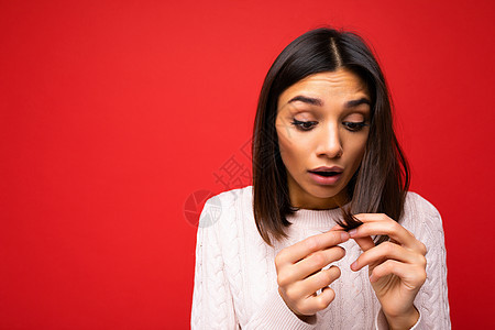 身着针织球衣的美丽震惊惊艳的黑发年轻女性的肖像 在红色背景中被隔离 有自由空间 摸着短发 头发分叉图片