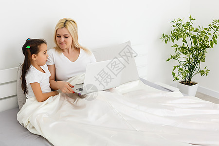 年幼母亲与幼儿一起在家床上在计算机上做家务的幼儿母性女士桌子互联网女孩孩子父母电脑女性人士图片