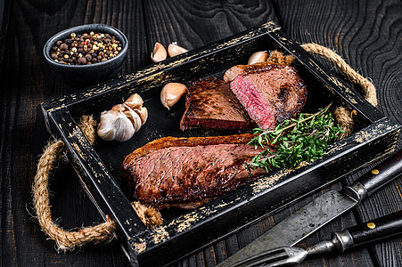 木制托盘中的烧烤烤臀盖或巴西 picanha 牛肉牛排 黑色的木制背景 顶视图香料胡椒食物木板鱼片炙烤牛扒红色大理石纹桌子图片