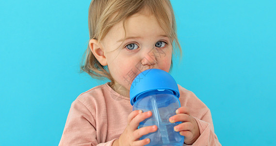 儿童饮用瓶装水孩子工作室几个月金发童年女孩杯子蓝色背景塑料图片